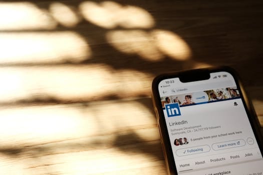 Close-up of a smartphone showing a LinkedIn profile page on a wooden table with shadows.